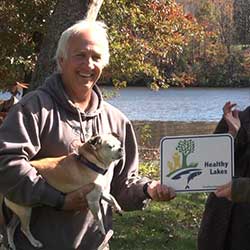 2015 Healthy Lakes Participant holds sign and dog along lakeshore